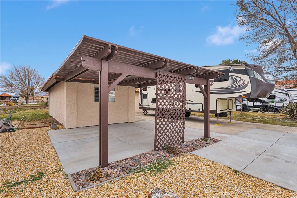 Covered concrete patio with a brown pergola roof and lattice screen beside a stucco building.