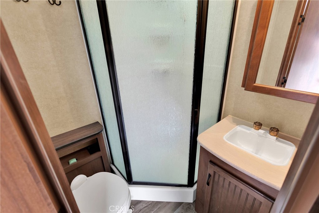 Compact bathroom with frosted-glass shower, toilet, and wood vanity with a white sink.