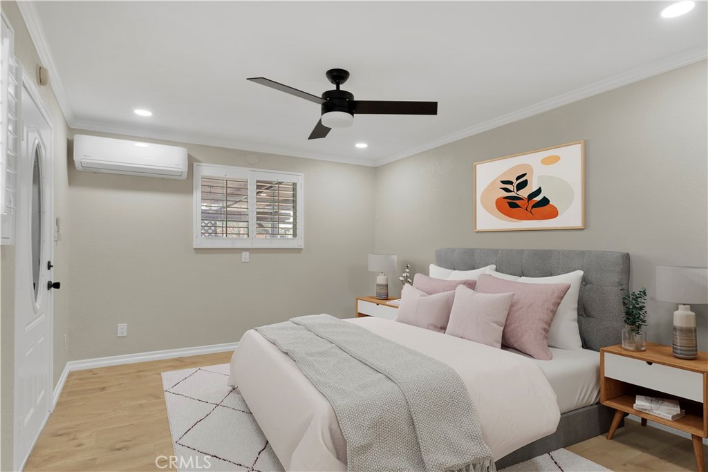 Bedroom with a gray upholstered headboard, blush pillows, ceiling fan and wall-mounted air conditioner.