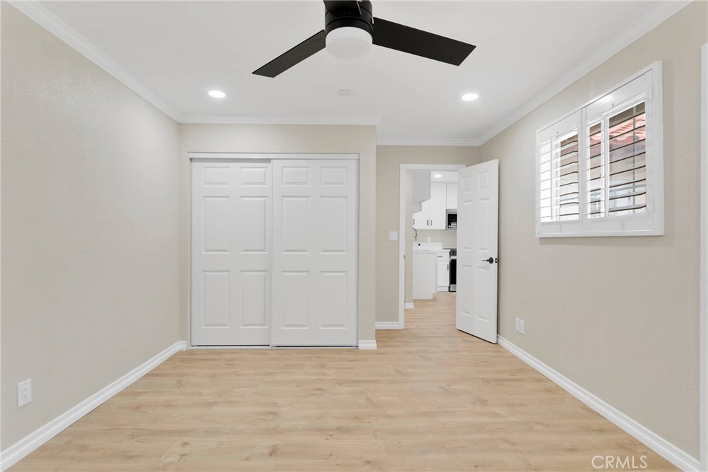 Empty bedroom with white closet doors, light wood-look flooring, and a shuttered window.