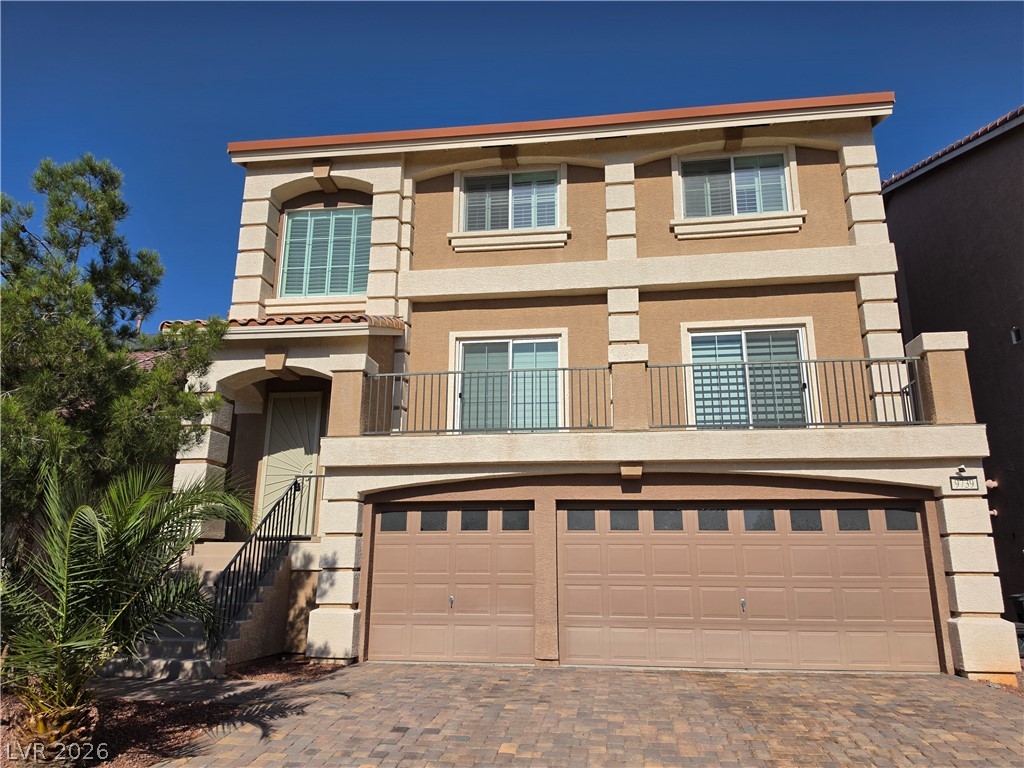 Two-story tan stucco home with a balcony, stone accents, and a wide double garage.