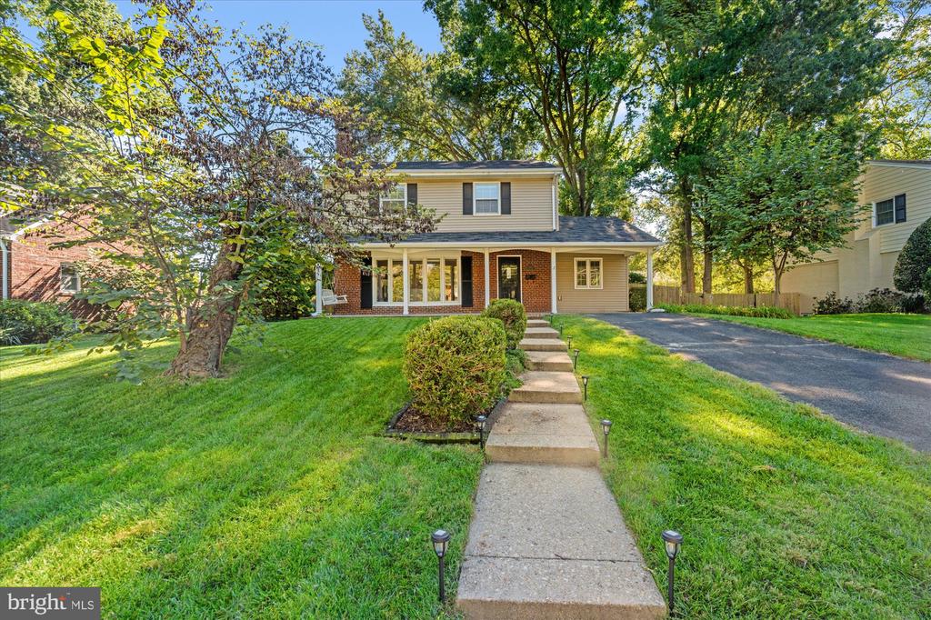 Two-story brick-and-siding home with a front walkway, driveway, and mature trees.