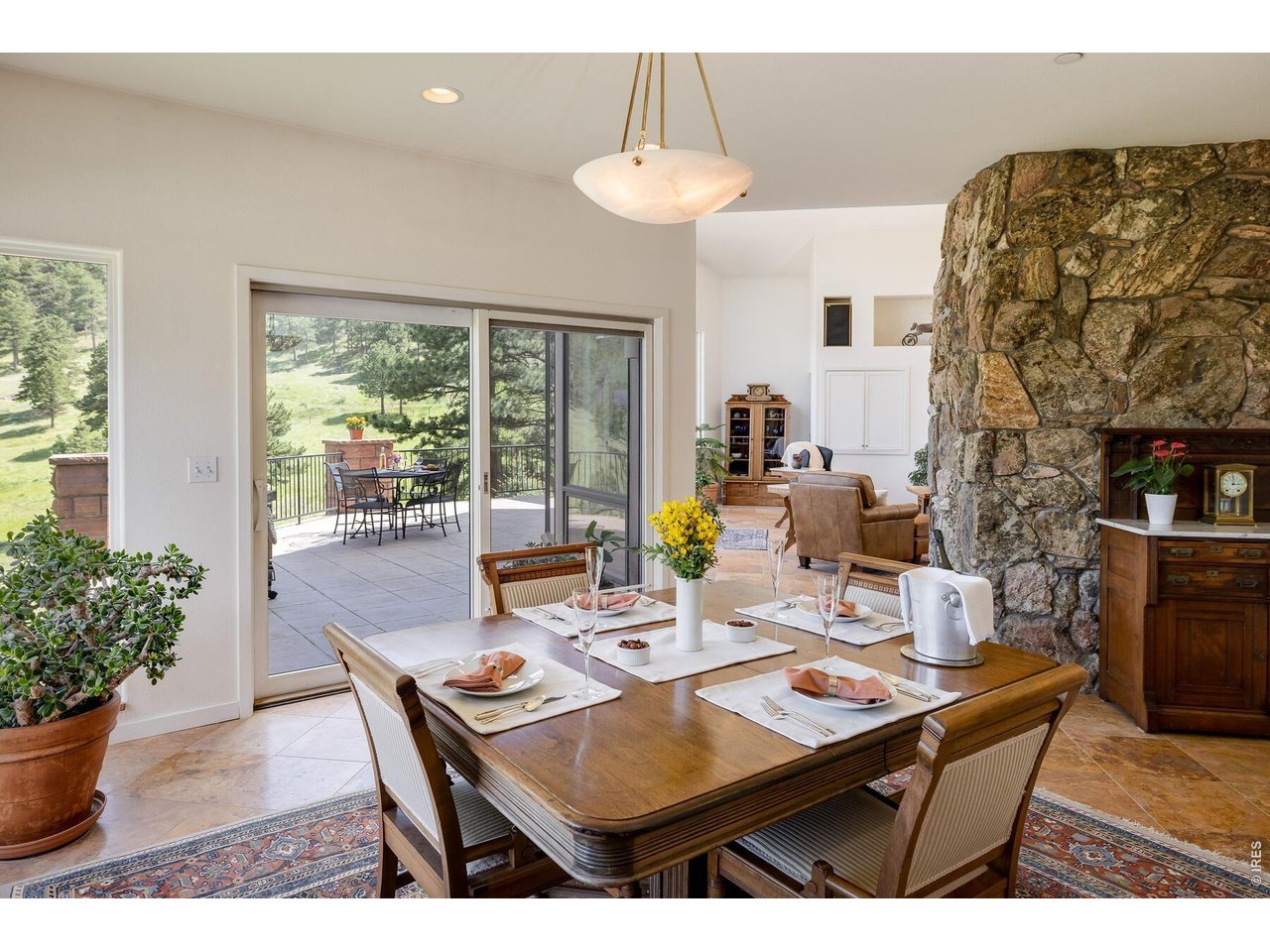 Dining room with a set wooden table, stone fireplace, and sliding doors opening to a patio.