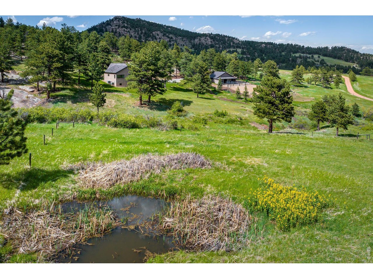 Rural property with two buildings, a pond, and wooded mountain slopes.