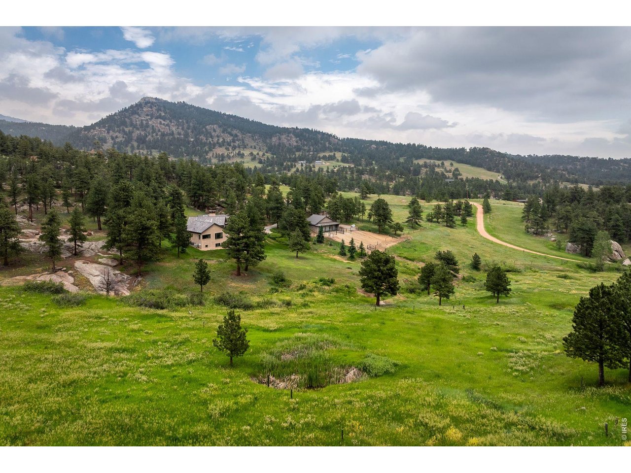 Rural property with a house, grassy acreage, pine trees, and a forested mountain view.