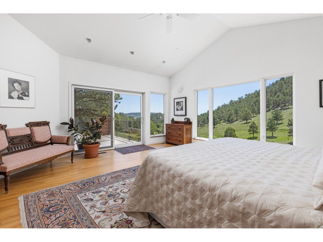 Bright bedroom with large windows overlooking a wooded hillside and a sliding door to the deck.
