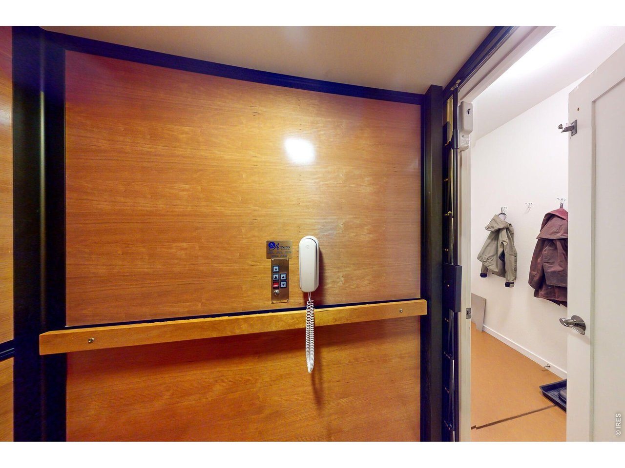 Wood-paneled elevator with a wall-mounted phone, open beside a coat area.