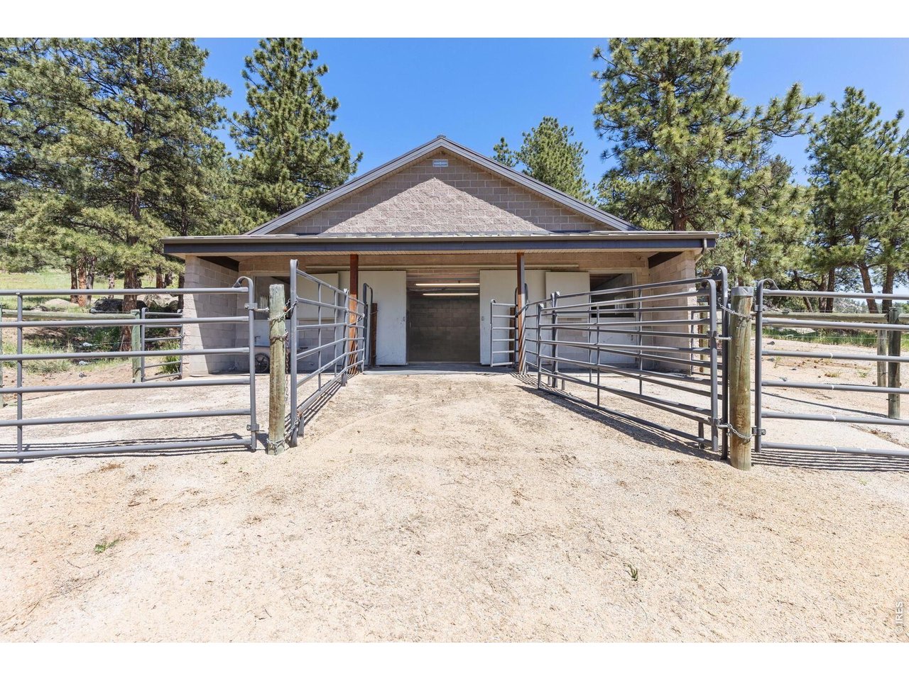 Masonry stable entrance framed by metal gates, with pine trees behind it.