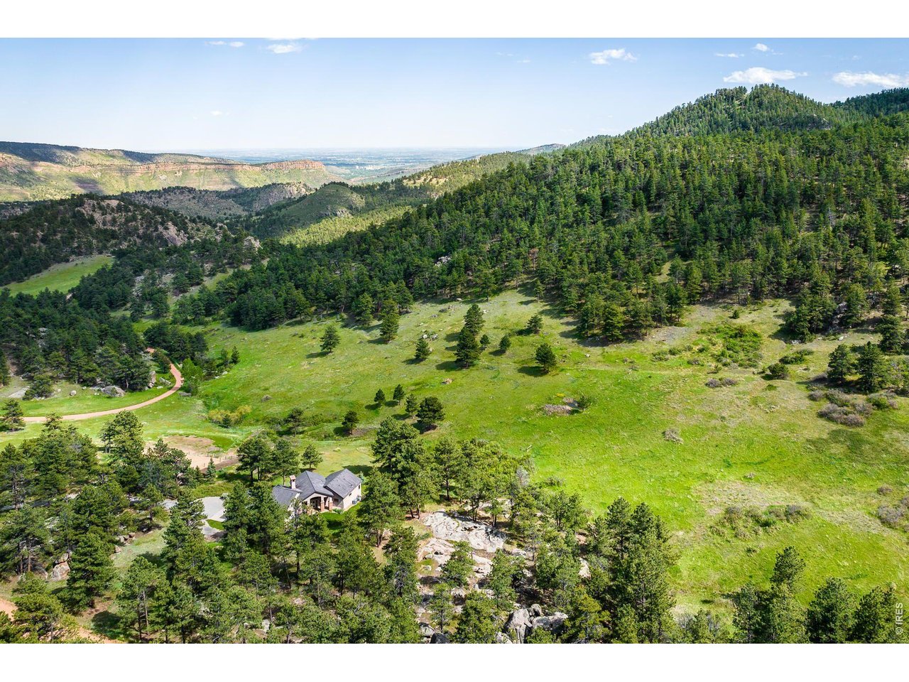 Aerial view of a home amid wooded hills, rocky outcrops, and a broad mountain valley.