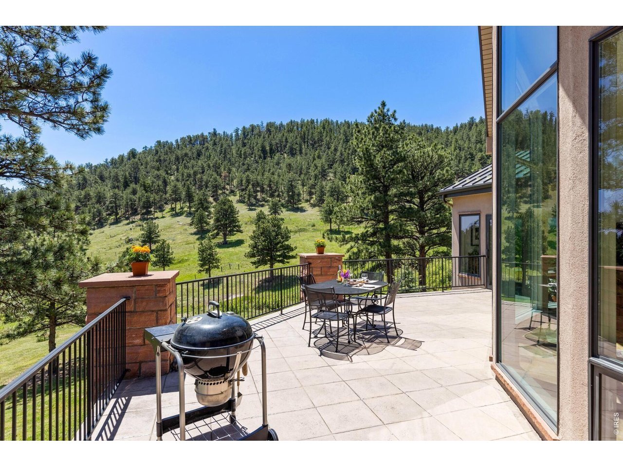 Paved patio with dining set and grill overlooking a pine-covered hillside.