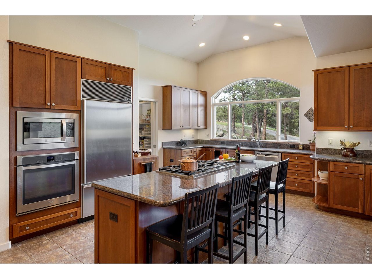 Kitchen with wood cabinetry, stainless steel appliances, and an island beneath an arched window.