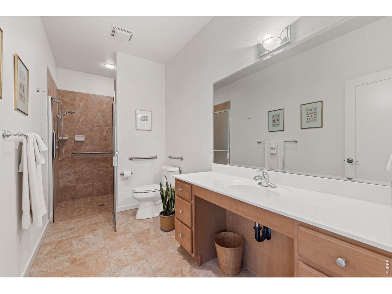 Bathroom with tiled walk-in shower, grab bars, and long wood vanity.