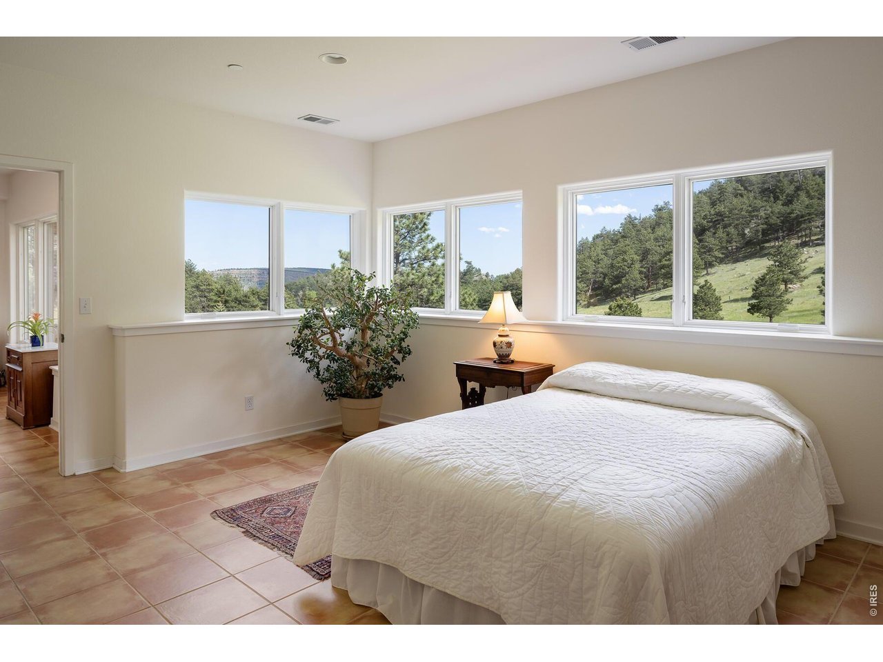 Bedroom with a white bed and large windows overlooking a wooded hillside.
