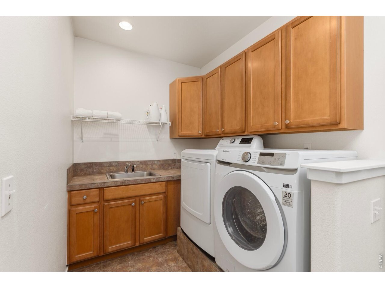 Laundry room with front-loading washer and dryer, wood cabinets, and a utility sink.