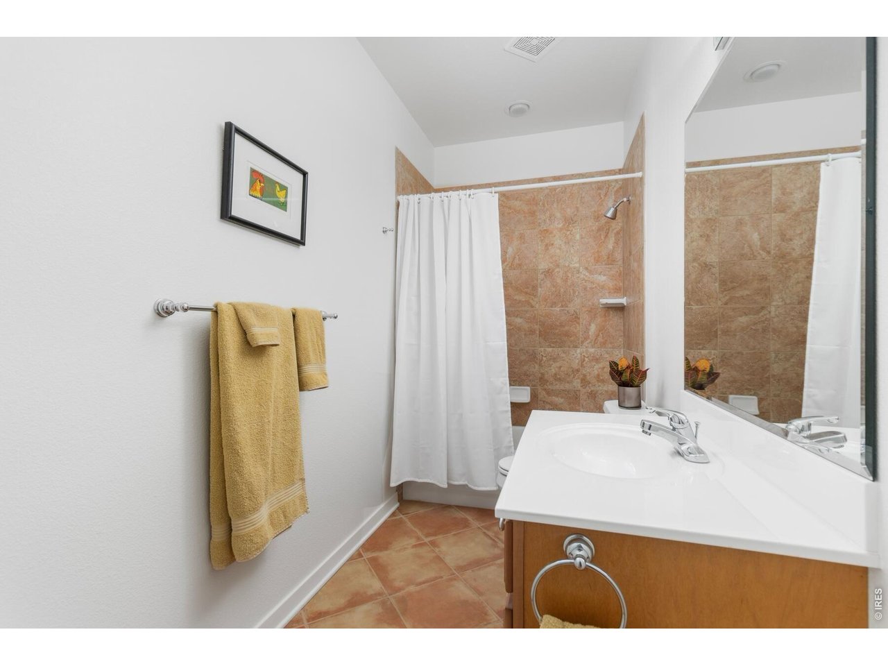Bathroom with tan tile, a white vanity and mirror, and towels hanging on a wall rack.