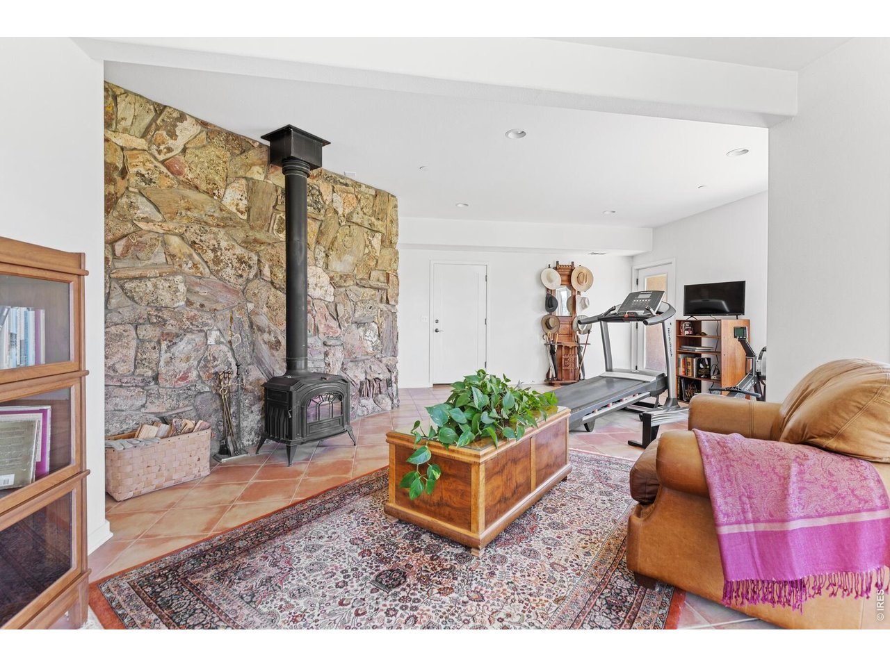 Living room with a stone wall and wood stove, treadmill, and leather seating.