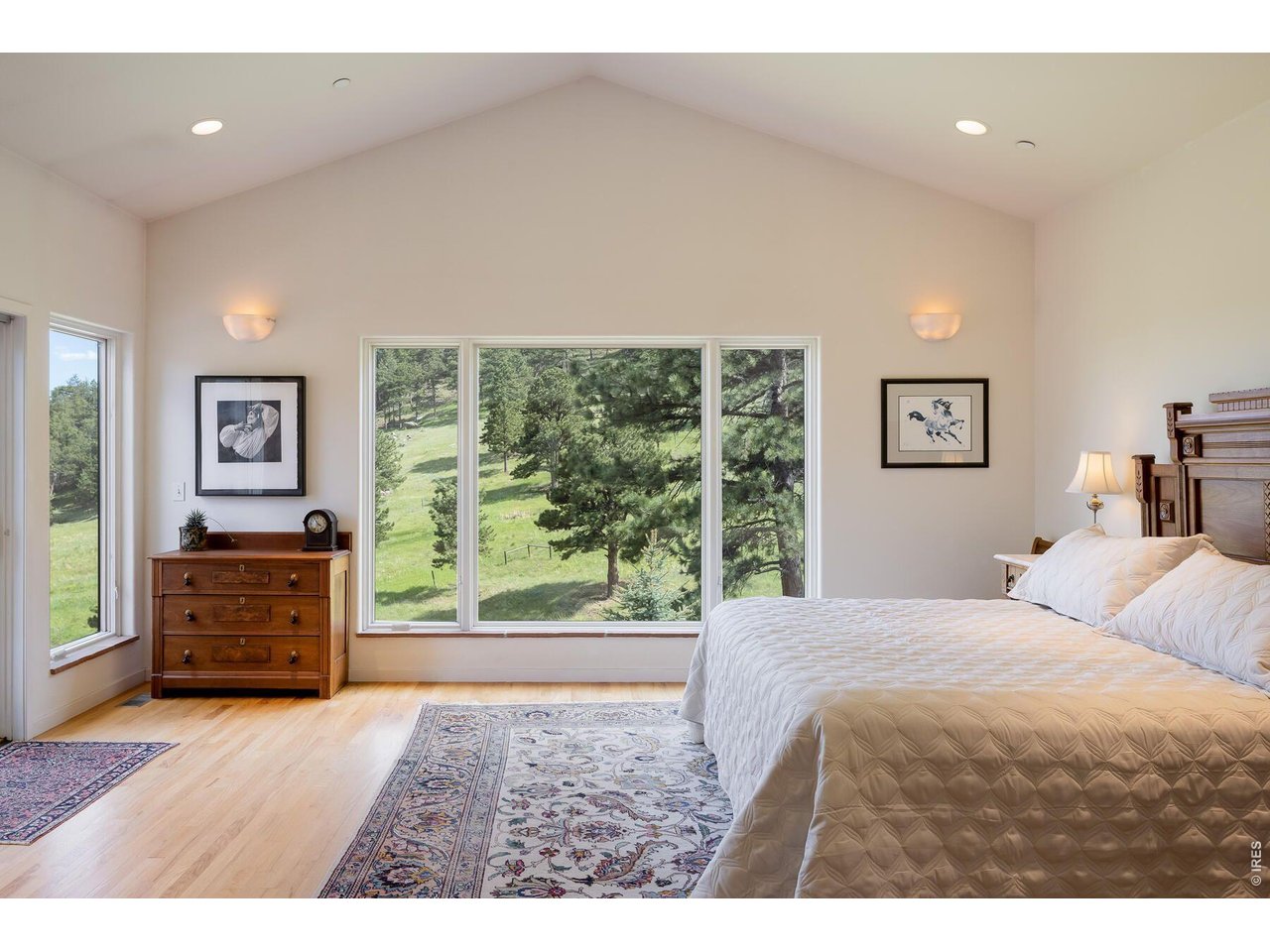 Furnished bedroom with a vaulted ceiling and broad windows overlooking a pine-covered hillside.