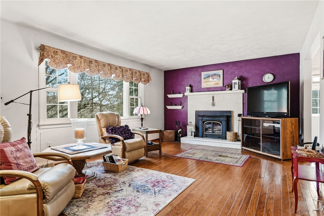 Living room with a purple accent wall, white brick fireplace, wood-burning stove, and hardwood floors.