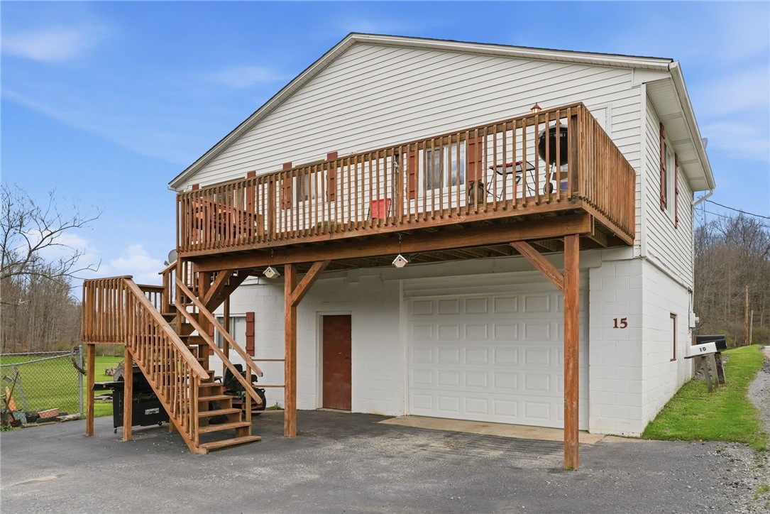 White two-story home with a raised wooden deck, exterior staircase, and garage beneath the deck.