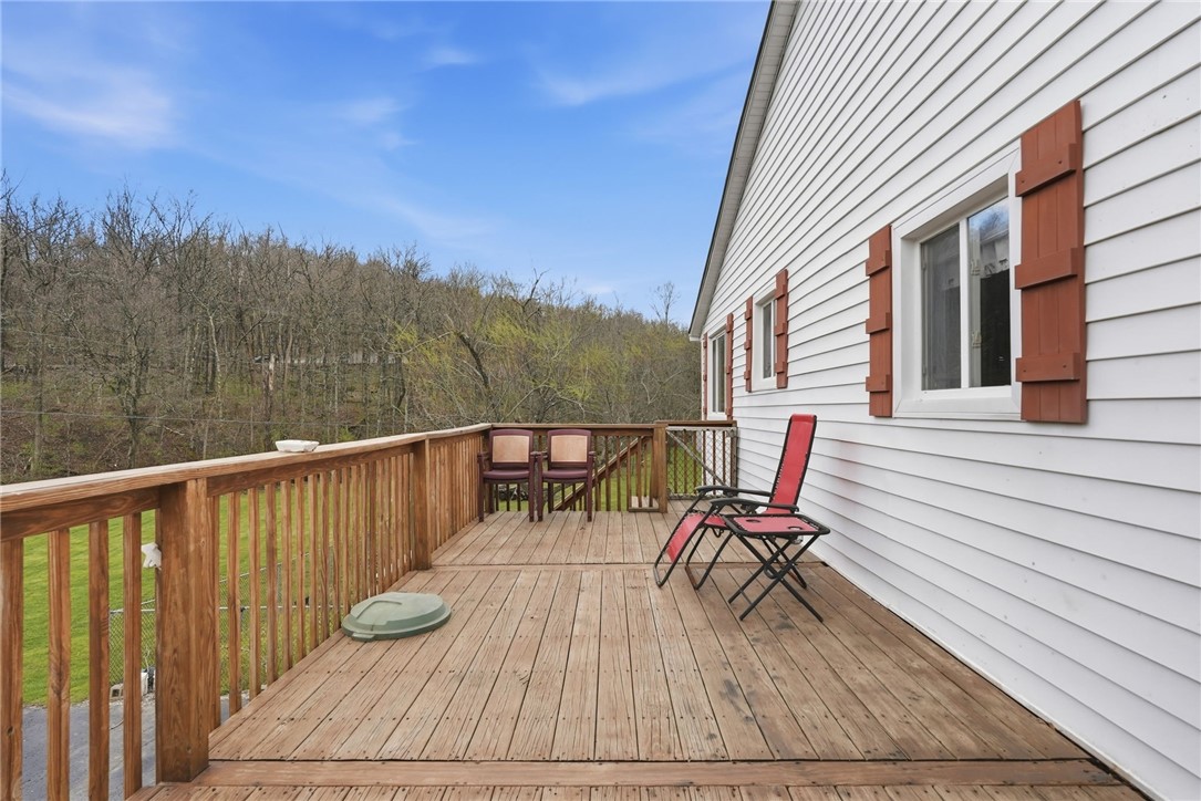 Wooden deck with red lounge chairs beside a white house, overlooking a wooded hillside.
