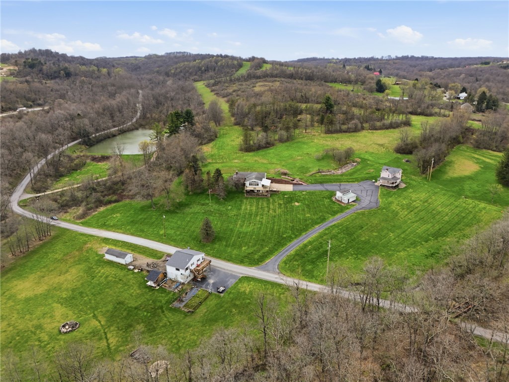 Aerial view of a rural property with green lawns, several buildings, a pond, and surrounding woodland.