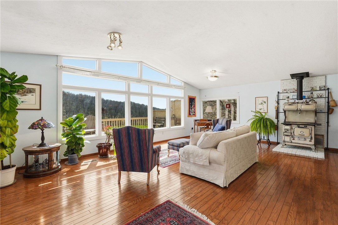 Living room with large tree-view windows, polished hardwood floors, a white sofa, and a vintage wood-burning stove.