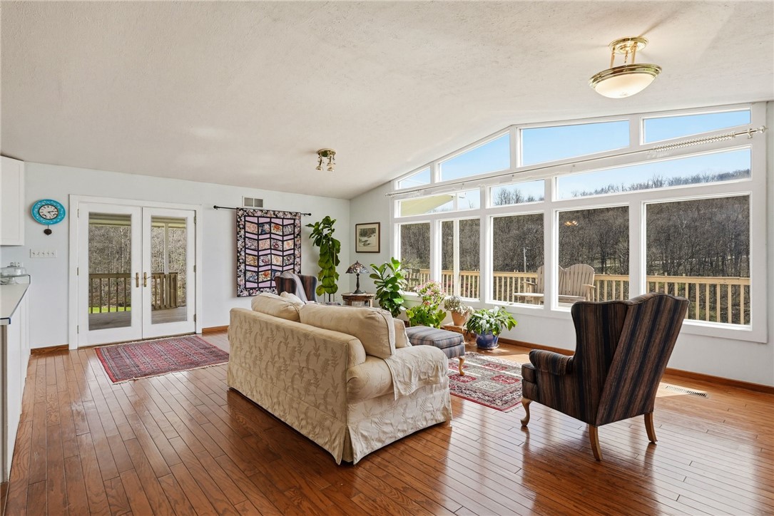 Living room with a vaulted ceiling, hardwood floors, and expansive windows overlooking trees.