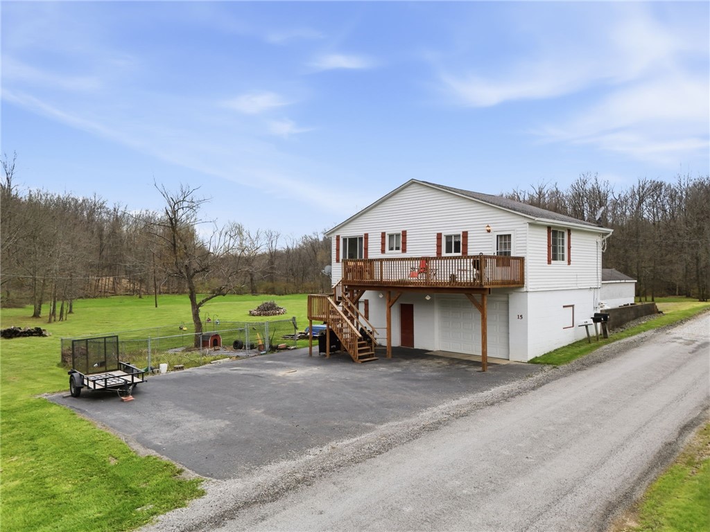 White two-story home with a raised wooden deck, garage, and broad green lawn beside a rural road.