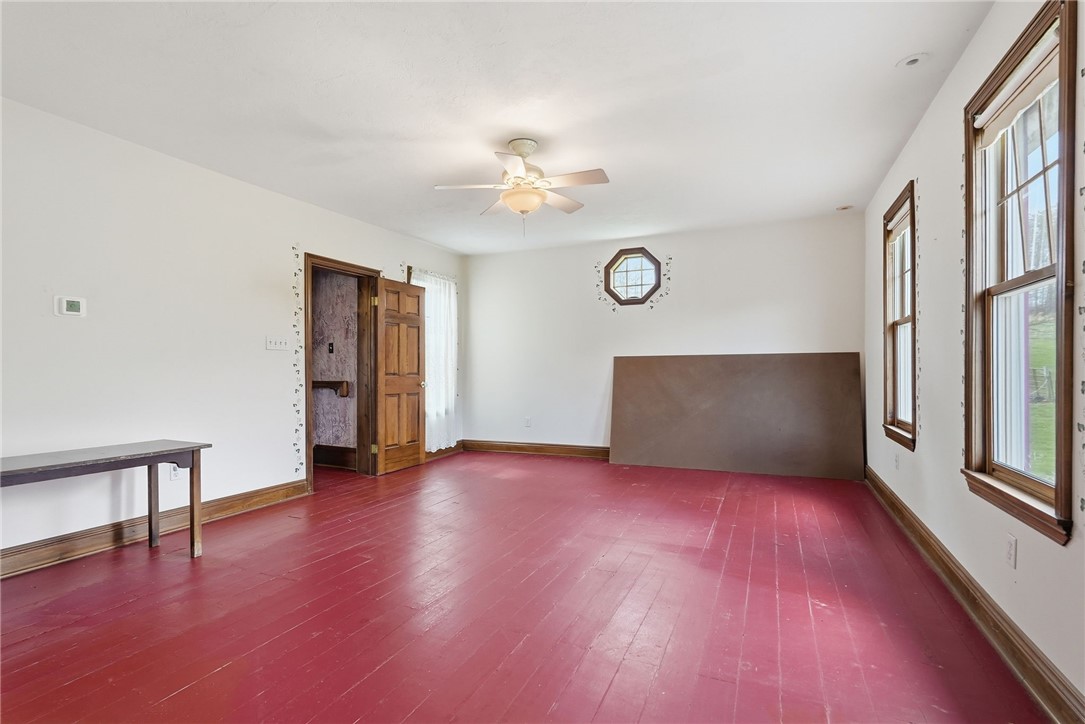 Mostly empty room with red-painted plank floors, wood trim, and an octagonal window.