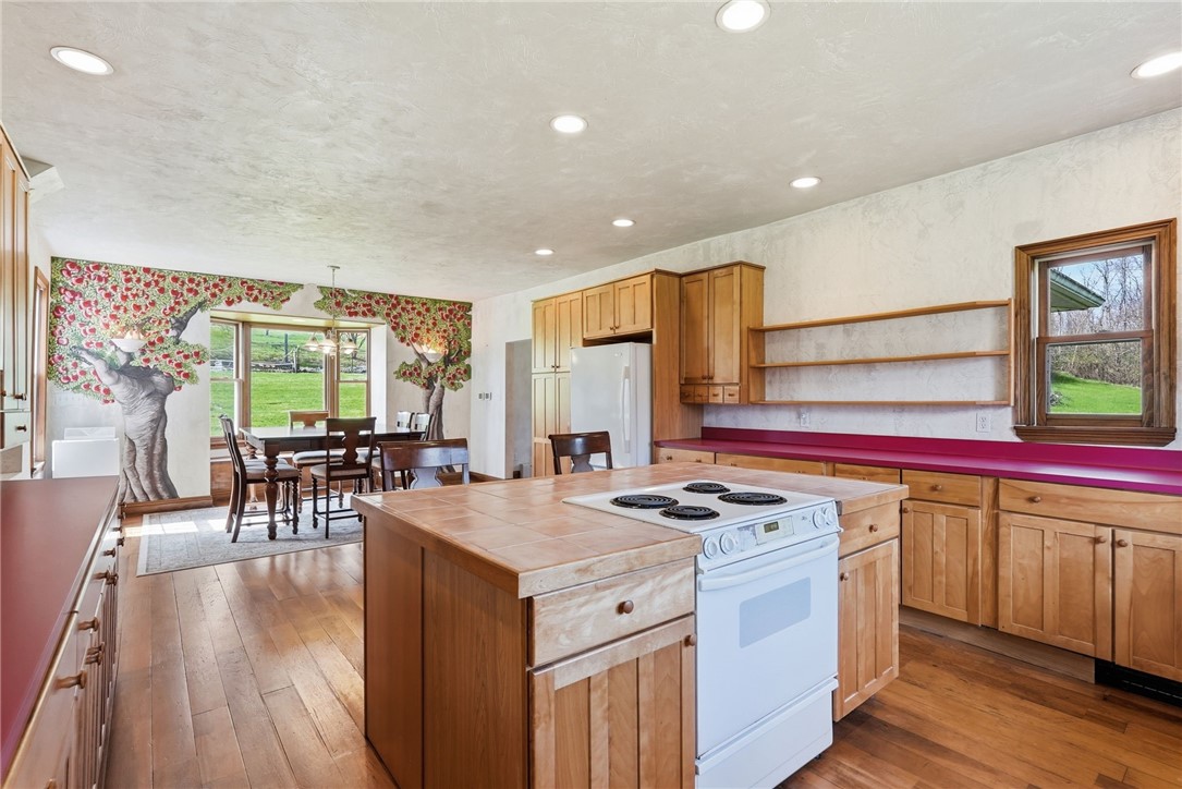Kitchen with a wood island and cooktop, opening to a dining area with a tree mural.