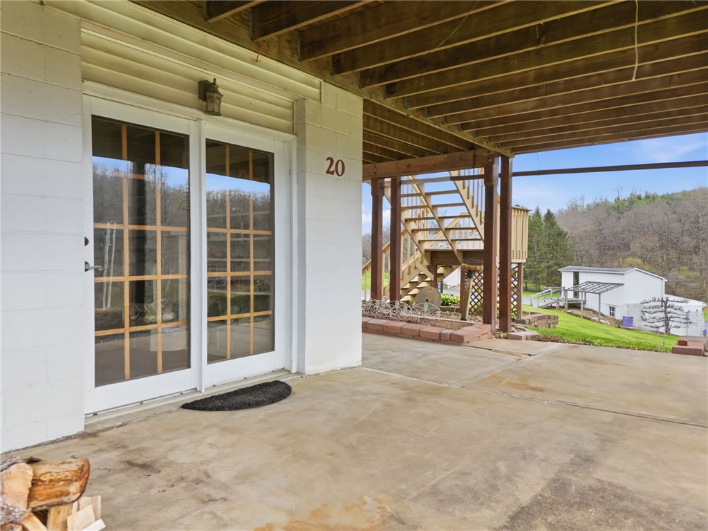 Covered concrete patio with sliding glass doors and a wooden staircase beside the home.