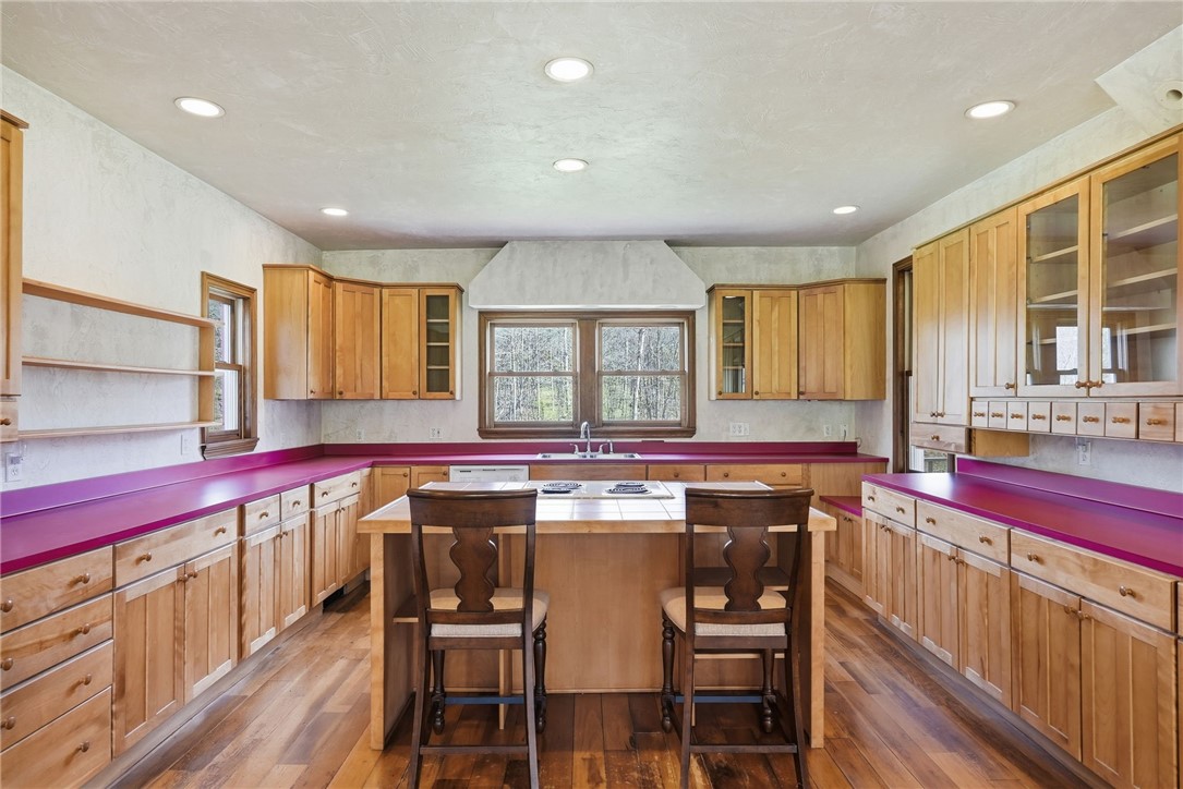Kitchen with magenta countertops, extensive wood cabinetry, and a central cooktop peninsula with two stools.