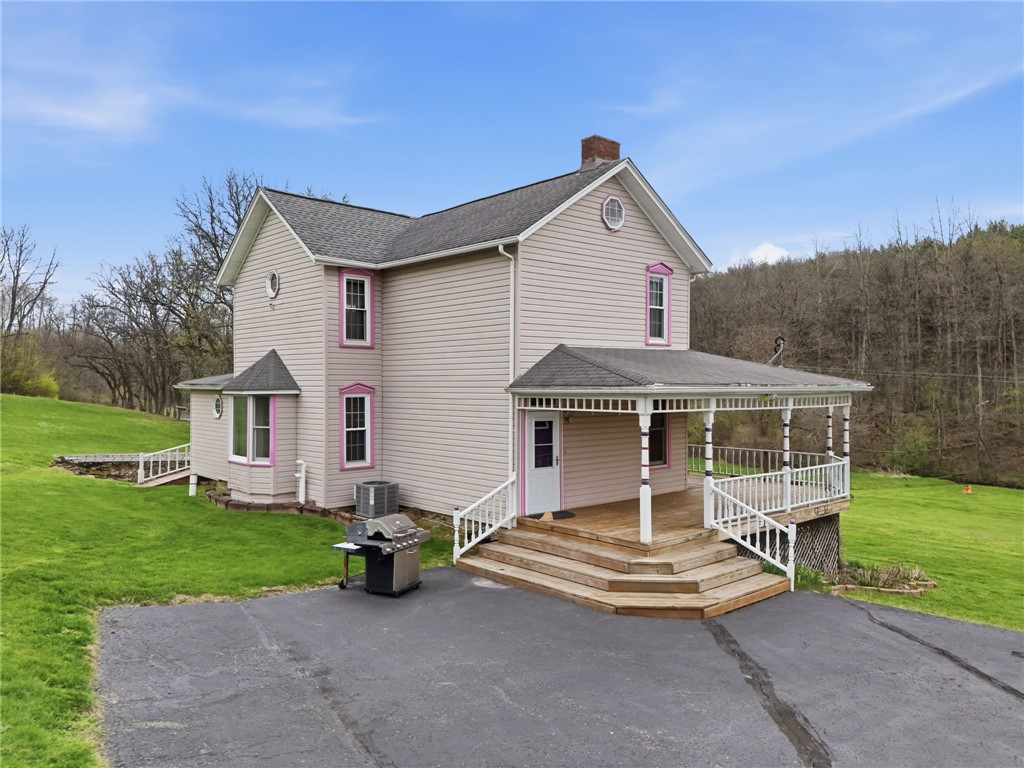 Two-story beige house with pink trim, a covered porch, wooden steps, and a broad paved driveway.