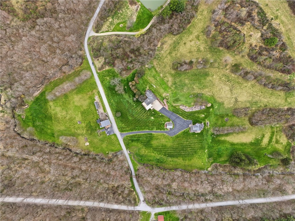 Aerial view of a home and outbuildings on a large grassy, wooded property.