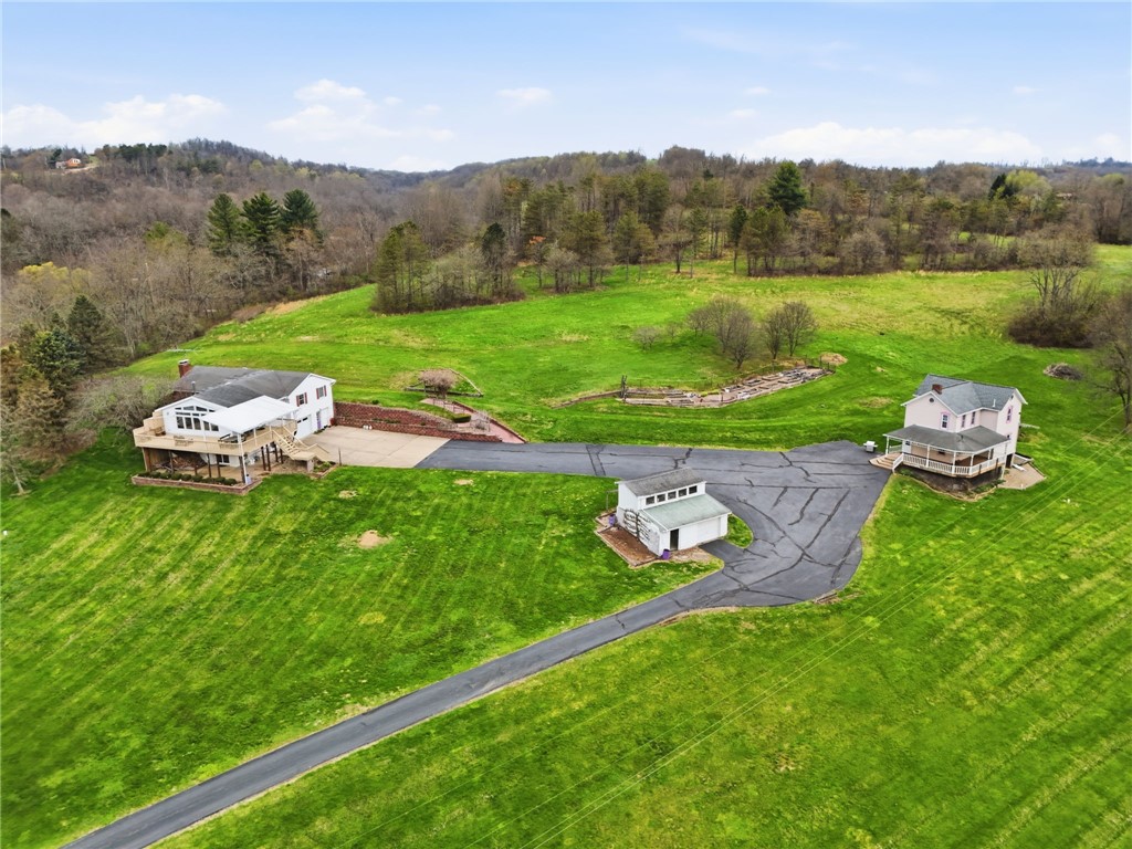 Aerial view of two homes, a detached garage, and a long driveway across a green rural property.