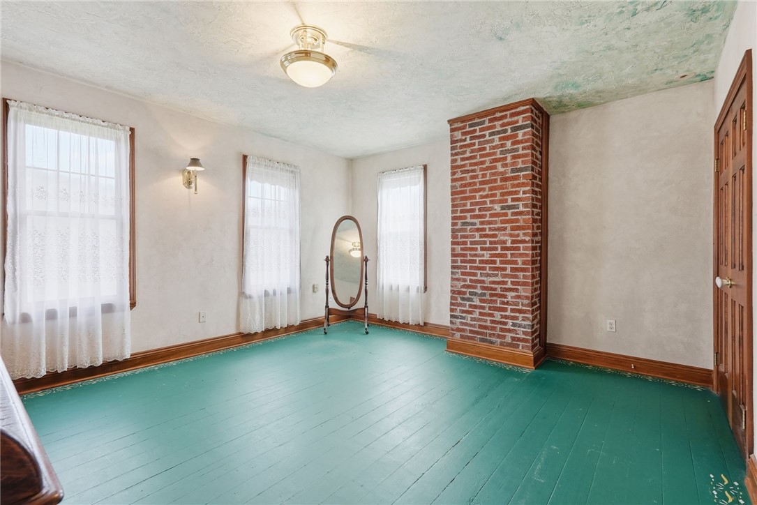 Vacant room with turquoise plank flooring, a brick chimney, lace-curtained windows, and an oval mirror.