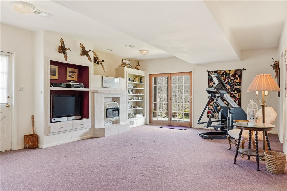 Furnished recreation room with a tiled fireplace, built-in television, French doors, and exercise machine.