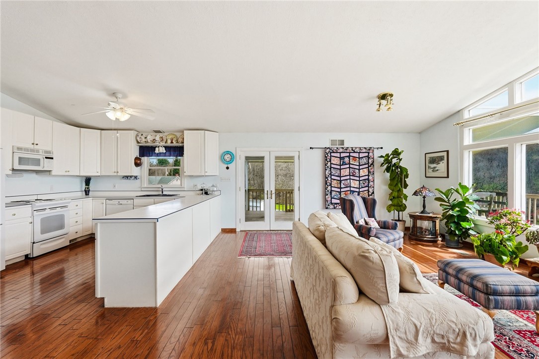 Open-plan kitchen and living room with white cabinetry, hardwood floors, and large windows.