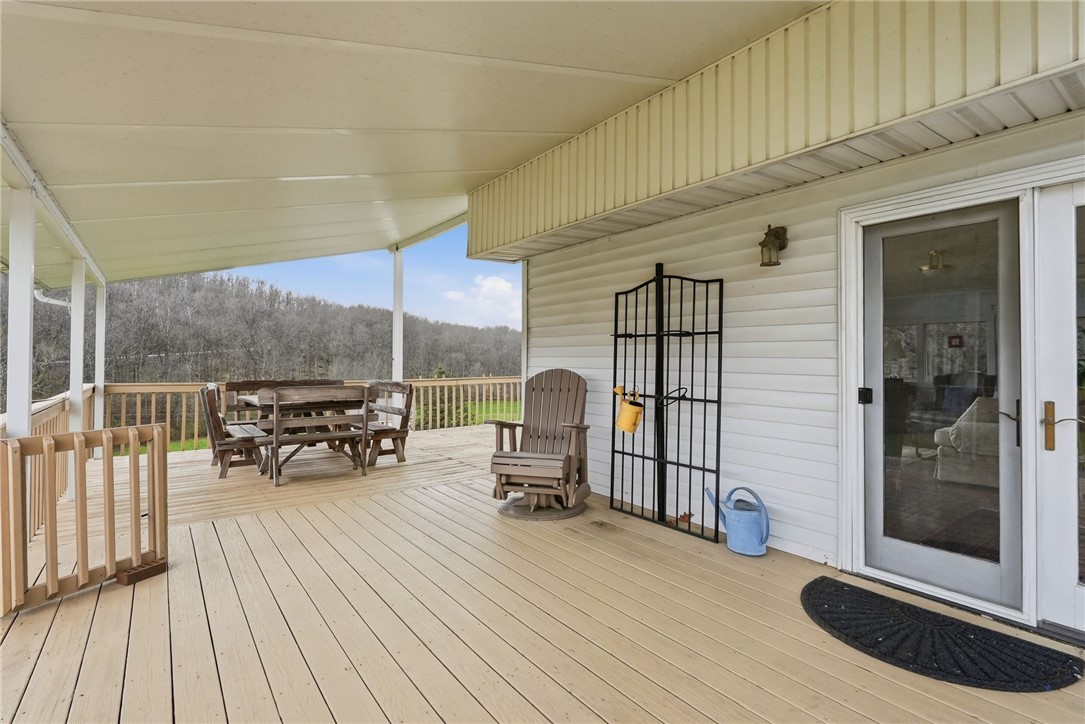 Covered deck with outdoor dining furniture and a wooded hillside view.