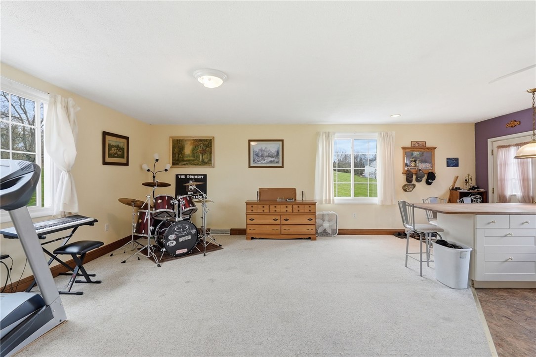 Carpeted bonus room with a drum kit, treadmill, keyboard, and dining area beside a kitchen island.