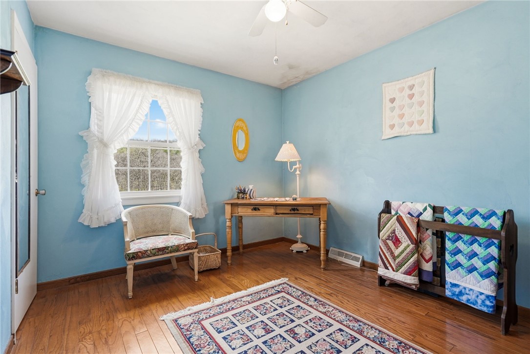 Blue-walled room with hardwood floors, a wooden desk, and colorful quilts on display.