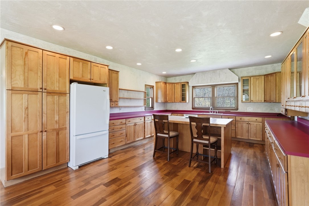 Kitchen with wood cabinets, burgundy counters, hardwood floors, and a central table with two stools.