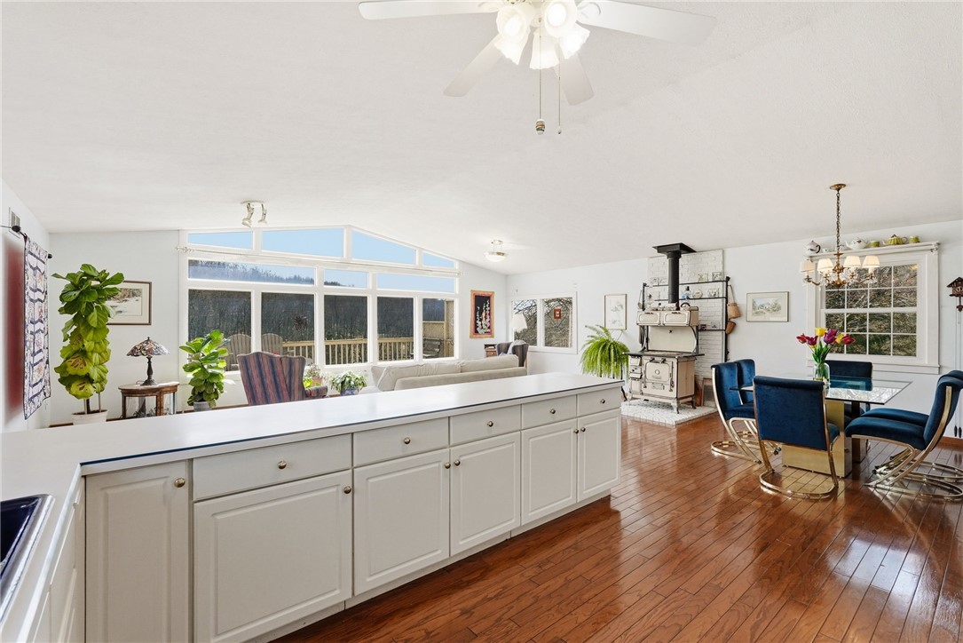 Open kitchen and dining area with white cabinetry, hardwood floors, and large windows overlooking trees.