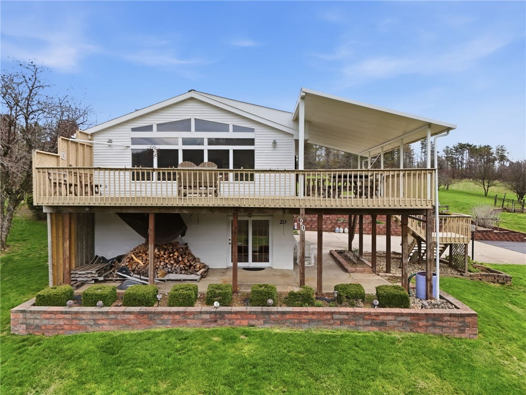 White house with a raised wooden deck, covered seating area, and landscaped lawn.