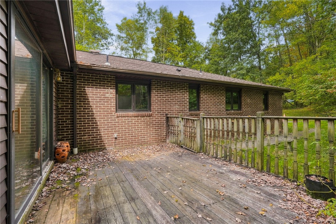 Weathered wooden deck beside a brick house, with a railing and sliding glass doors.