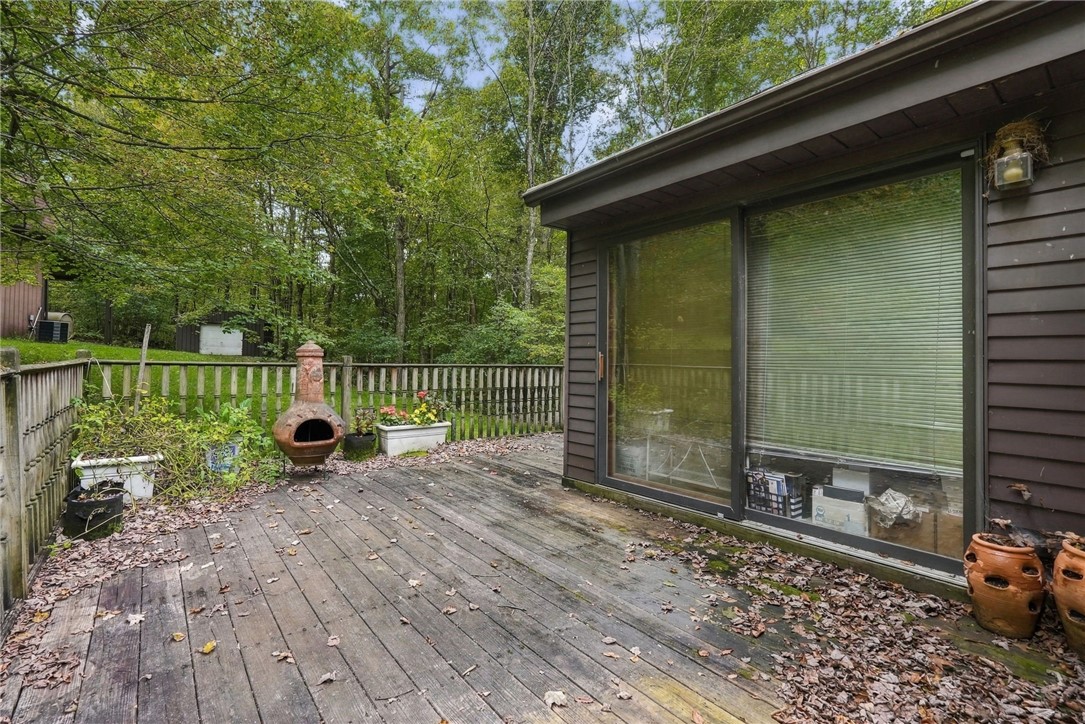 Wooden deck beside sliding glass doors, with potted plants and a chiminea overlooking a wooded yard.