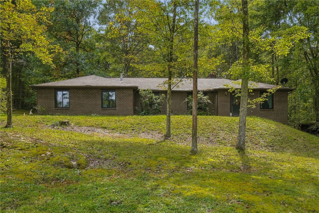 Single-story brick house on a sloping lawn, surrounded by mature trees.
