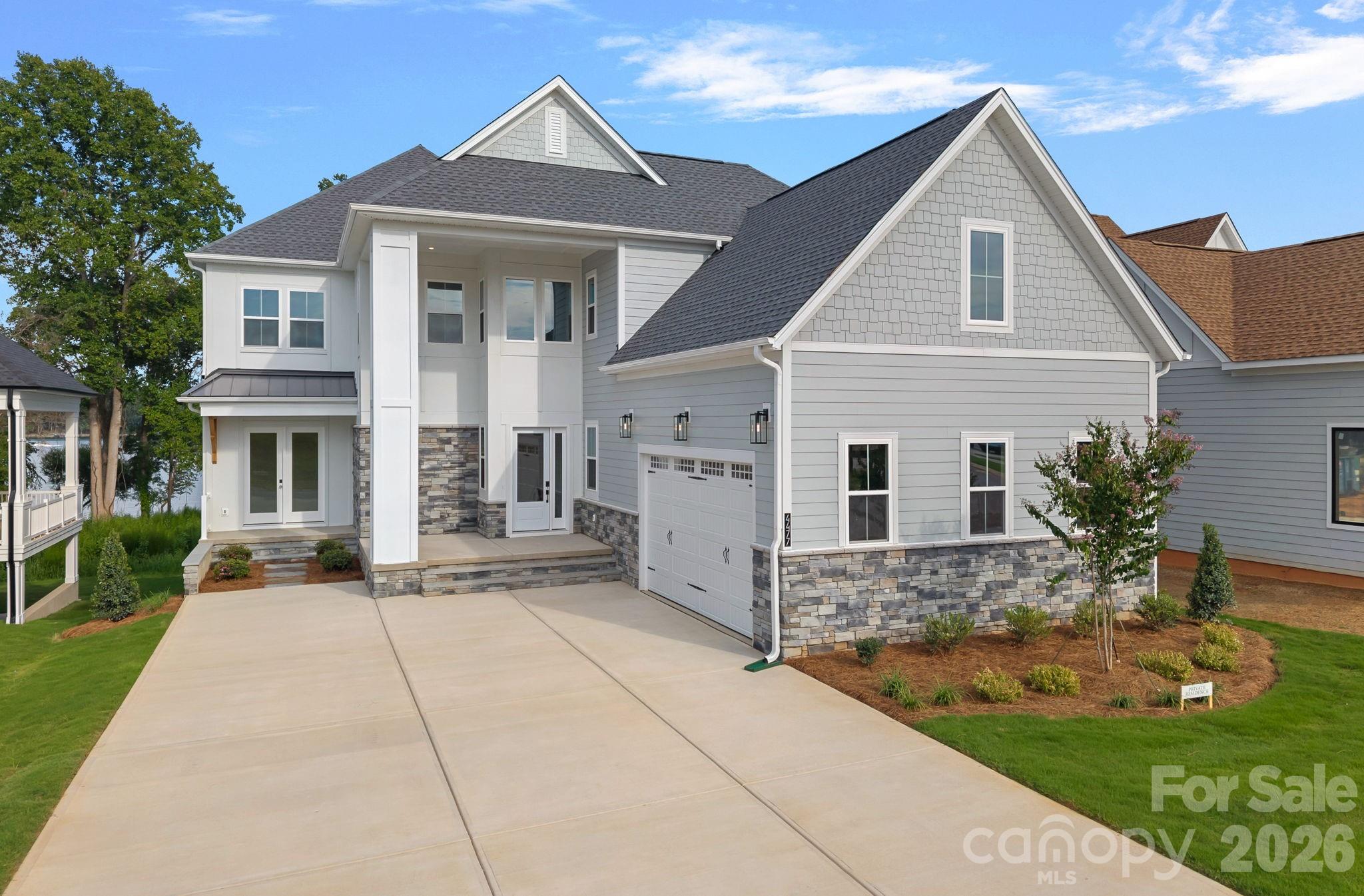 Gray two-story house with stone accents, multiple gables, an attached garage, and a broad driveway.