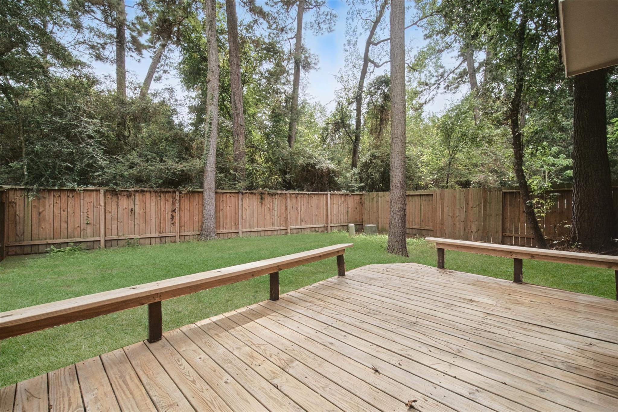 Wooden deck overlooking a fenced grassy backyard shaded by tall trees.