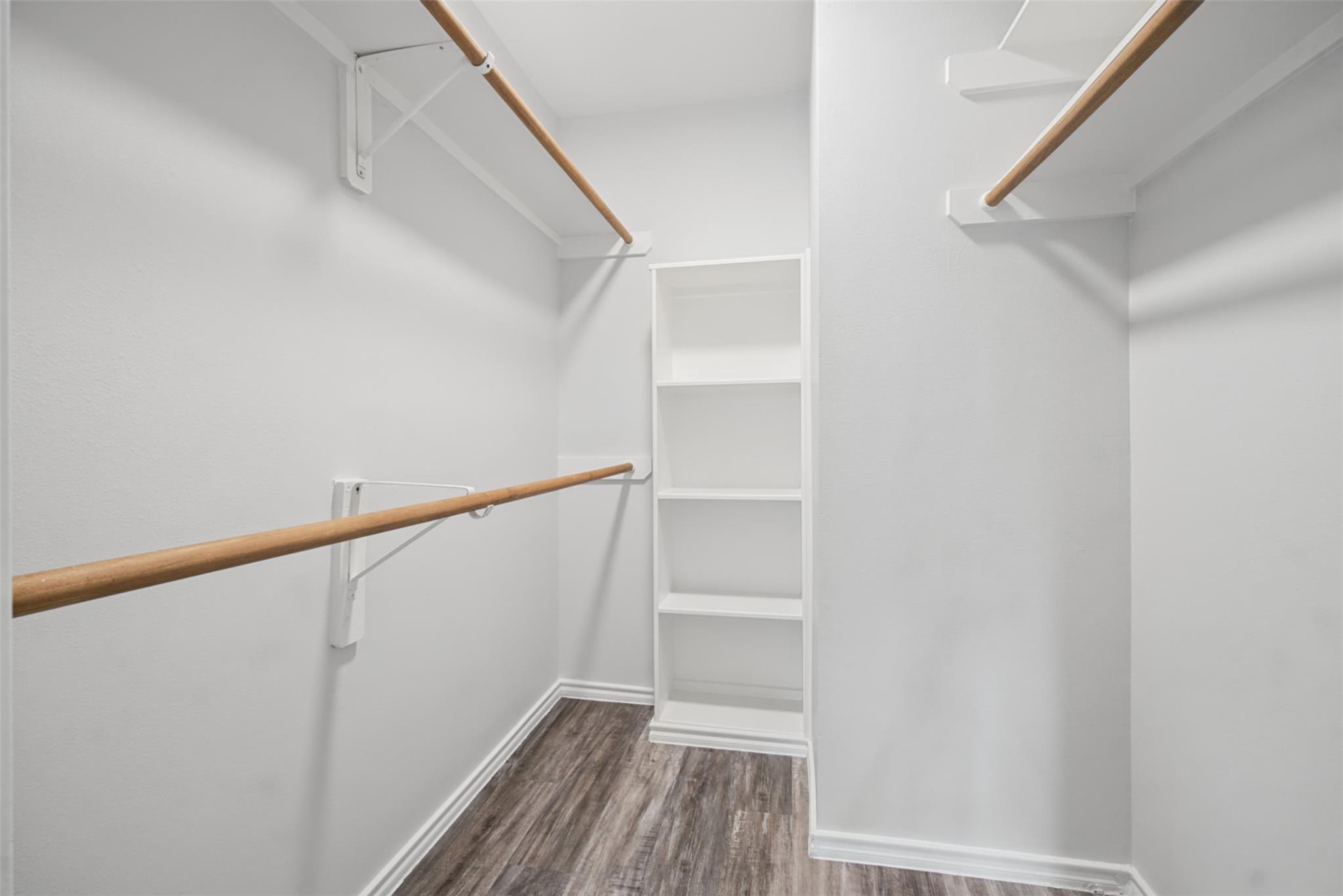 Walk-in closet with wooden hanging rods, built-in shelving, and dark wood-look flooring.